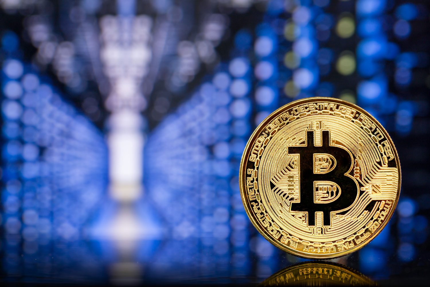 Close-up of a metallic golden Bitcoin cryptocurrency coin standing on a computer board against the backdrop of the colorful lights of a mining farm